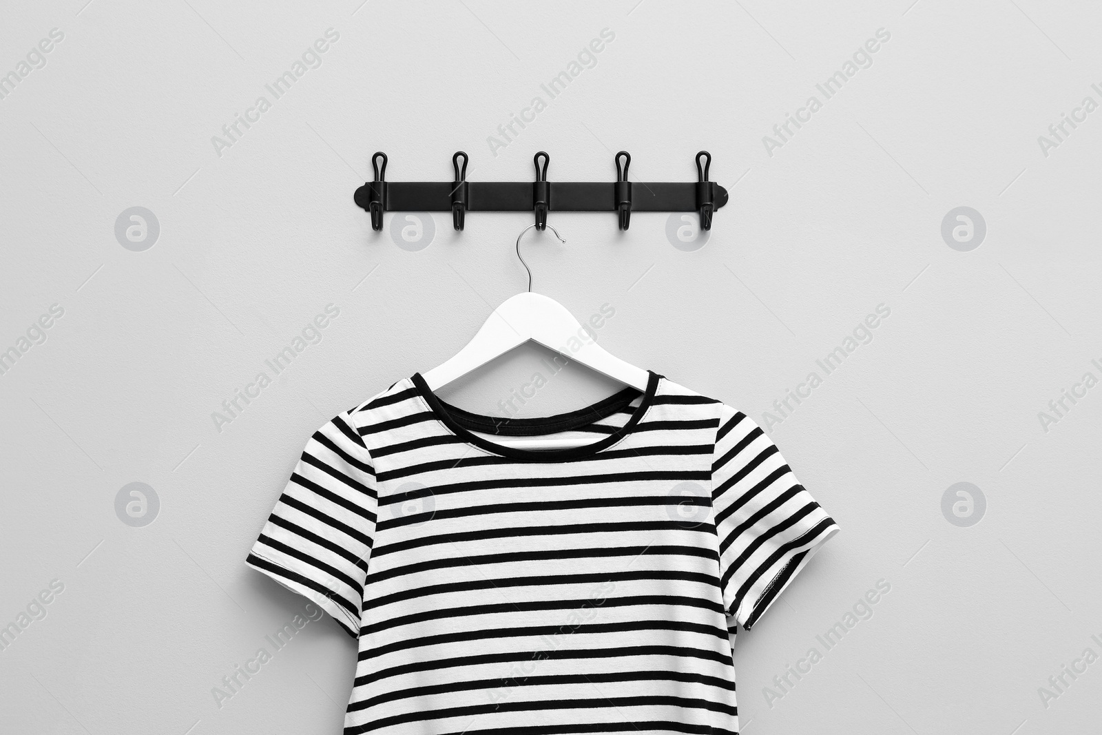 Photo of Hanger with striped T-shirt on light grey wall