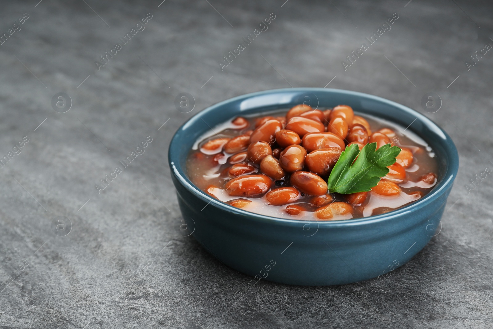 Photo of Bowl of canned kidney beans with parsley on grey table, closeup. Space for text