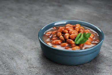 Photo of Bowl of canned kidney beans with parsley on grey table, closeup. Space for text
