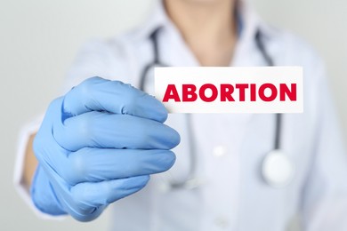 Image of Doctor holding paper card with word Abortion on light grey background, closeup