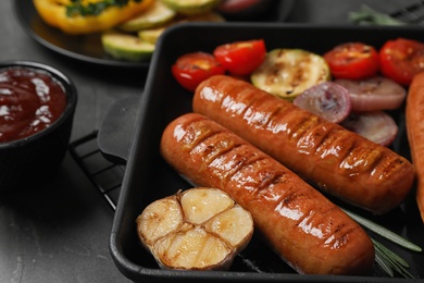 Photo of Delicious grilled sausages and vegetables on grey table, closeup