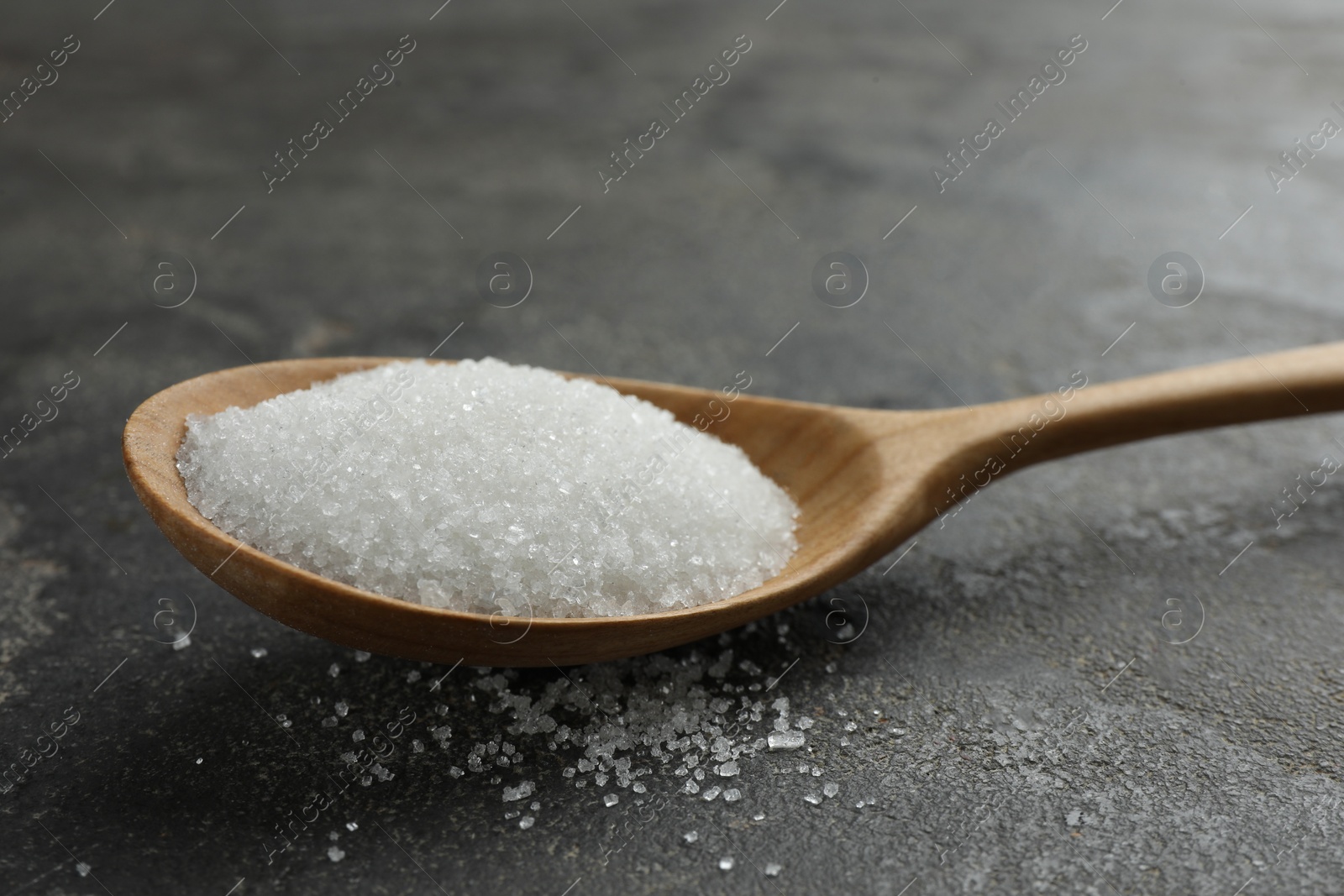 Photo of Spoon with granulated sugar on grey textured table, closeup
