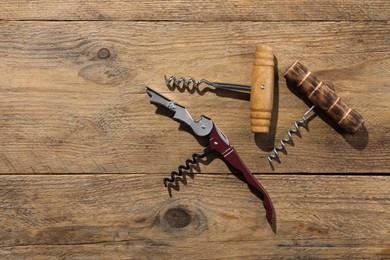 Different corkscrews on wooden table, flat lay. Space for text