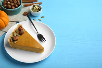 Photo of Piece of delicious pumpkin pie with hazelnuts, seeds and fork on light blue wooden table, space for text
