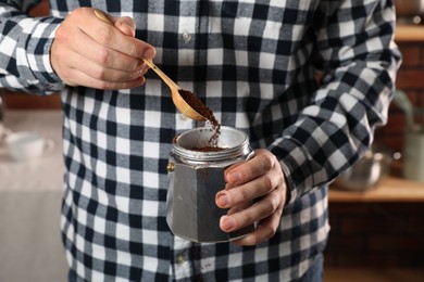 Photo of Man putting ground coffee into moka pot indoors, closeup