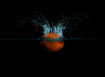 Photo of Grapefruit falling down into clear water against black background