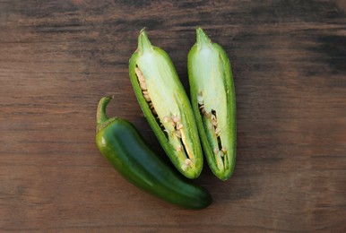 Photo of Whole and cut green chili peppers on wooden table, flat lay