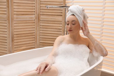Beautiful woman taking bath with foam in tub indoors, space for text