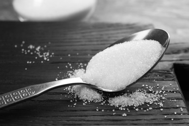 Photo of Spoon with granulated sugar on black wooden board, closeup