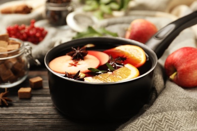 Photo of Saucepan with tasty mulled wine on black wooden table