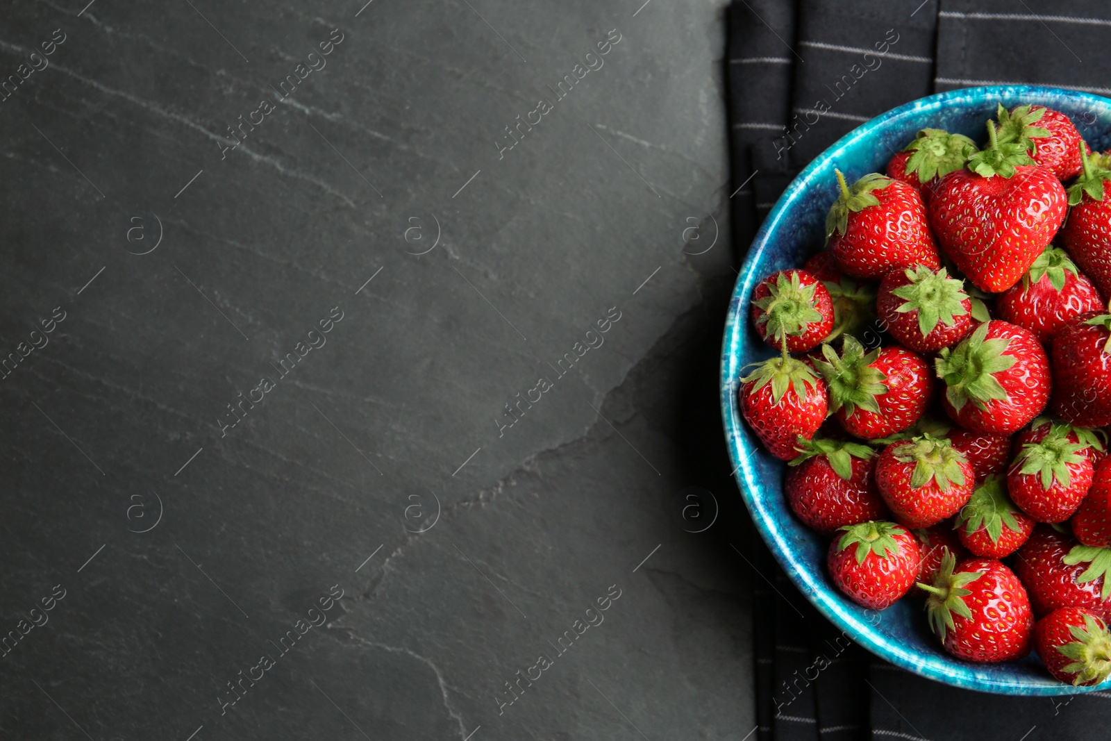 Photo of Delicious ripe strawberries in bowl on black table, flat lay. Space for text