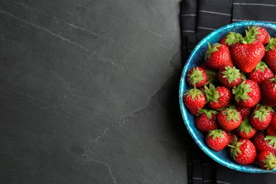 Photo of Delicious ripe strawberries in bowl on black table, flat lay. Space for text
