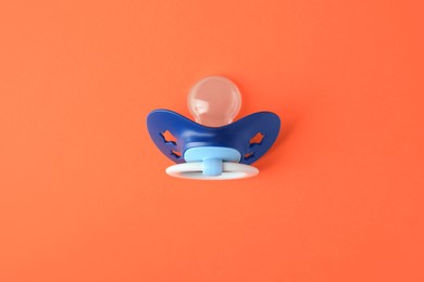 Photo of One blue baby pacifier on orange background, top view