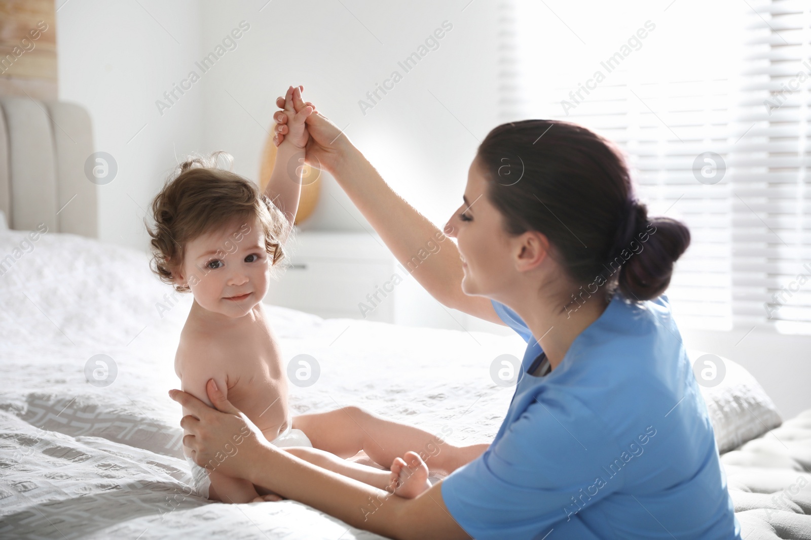 Photo of Orthopedist examining little baby on bed indoors