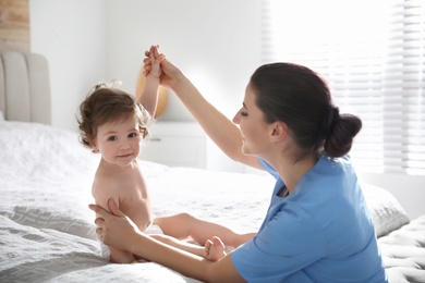 Photo of Orthopedist examining little baby on bed indoors