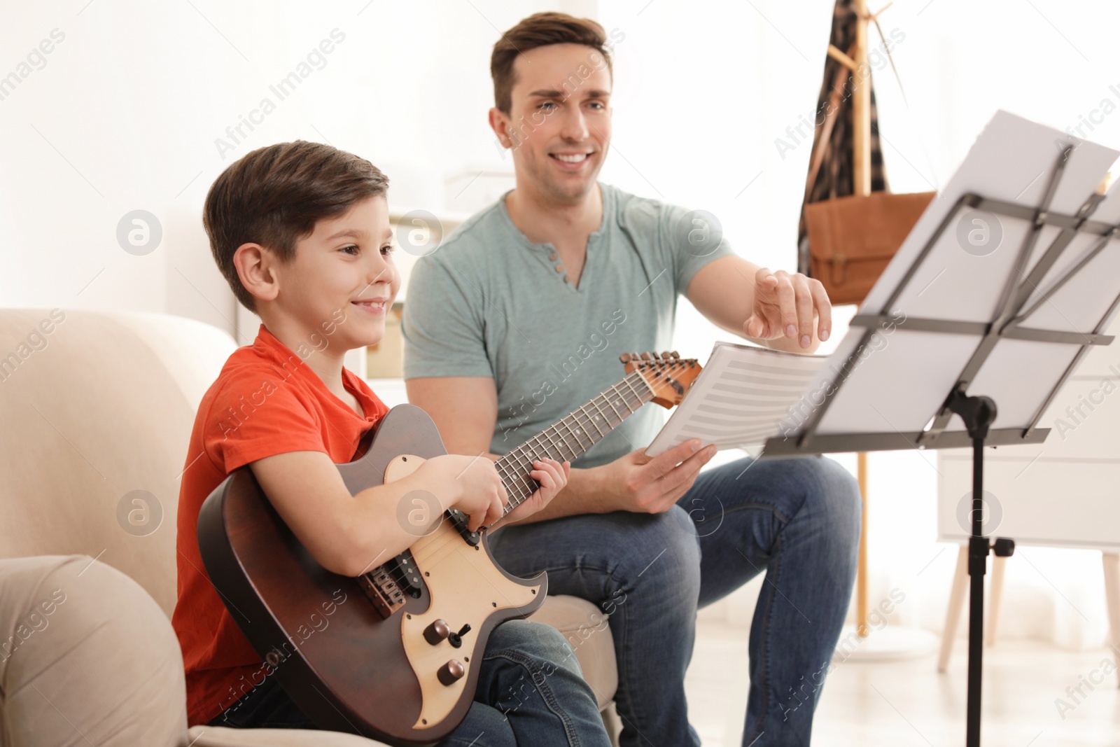 Photo of Little boy playing guitar with his teacher at music lesson. Learning notes