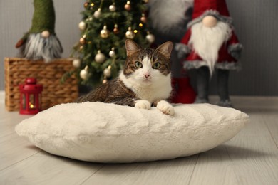 Photo of Cute cat lying on soft pillow near Christmas decor at home. Adorable pet