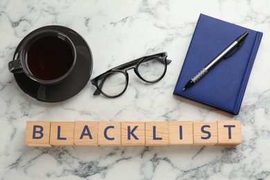 Photo of Wooden cubes with word Blacklist, cup of coffee and office stationery on white marble table, flat lay
