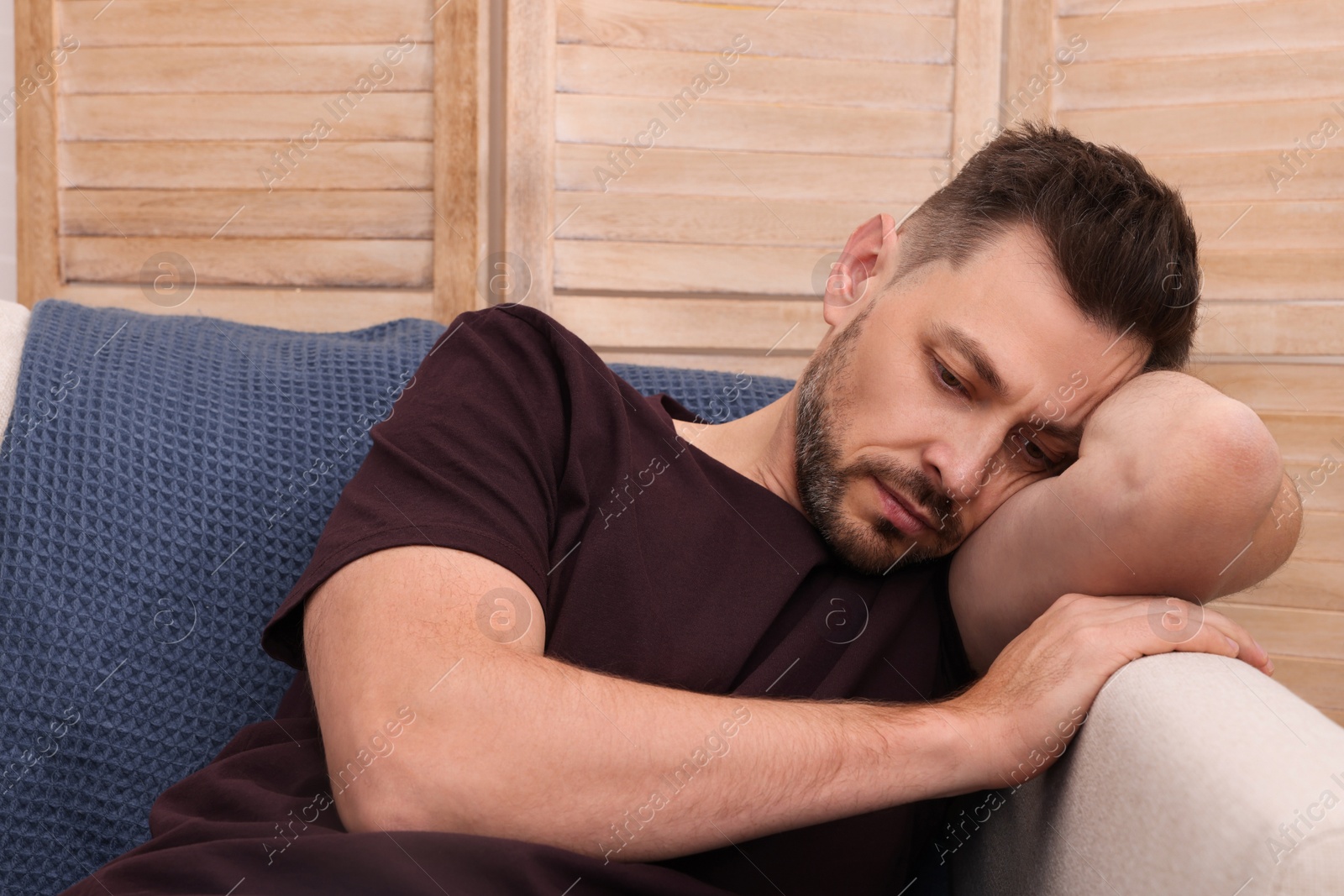 Photo of Upset man sulking on sofa at home. Loneliness concept