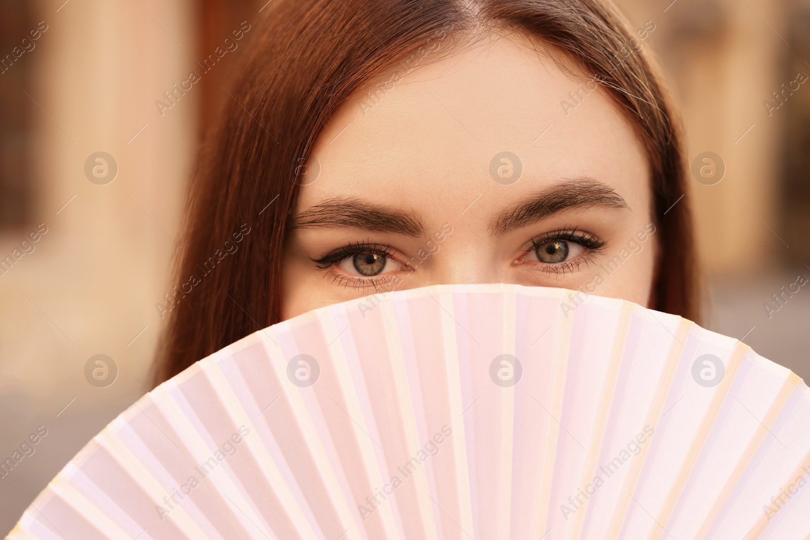 Photo of Young woman holding hand fan outdoors, closeup