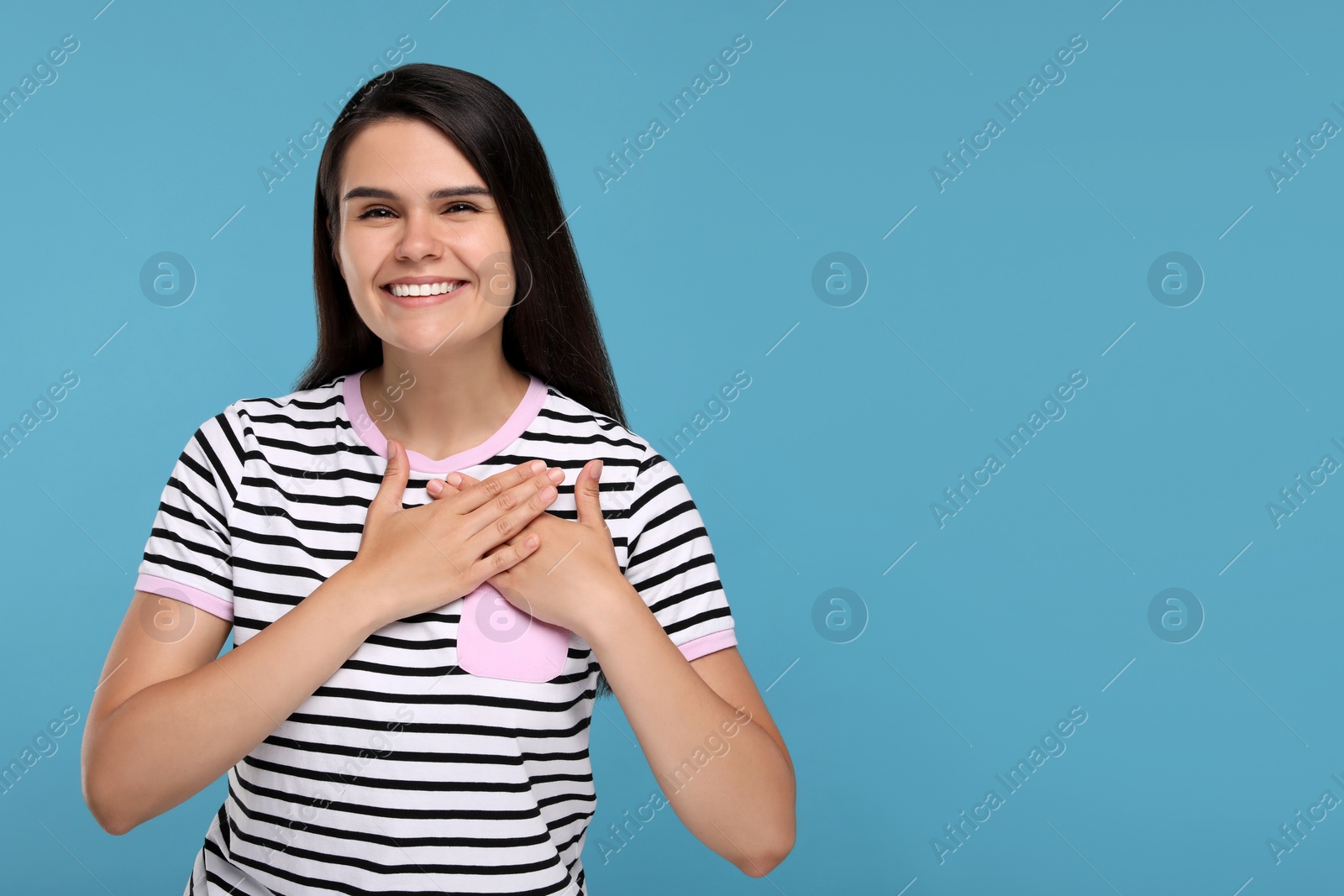 Photo of Thank you gesture. Beautiful grateful woman holding hands near heart on light blue background, space for text
