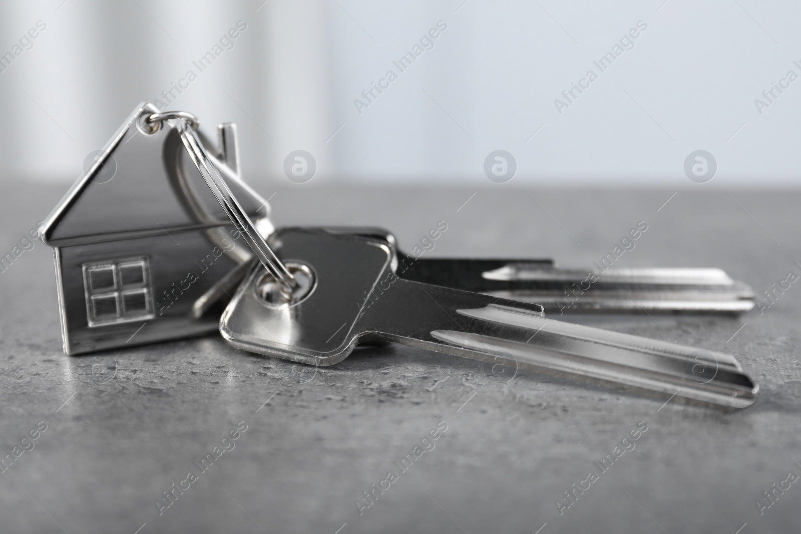 Photo of Keys with keychain in shape of house on grey textured table indoors, closeup