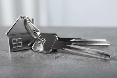Photo of Keys with keychain in shape of house on grey textured table indoors, closeup