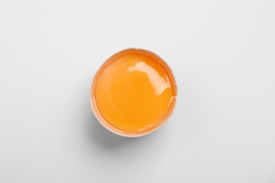 Photo of Cracked eggshell with raw yolk on white background, top view