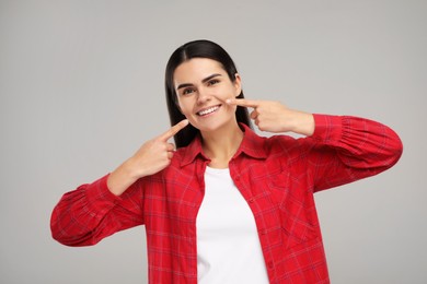 Young woman showing her clean teeth and smiling on light grey background