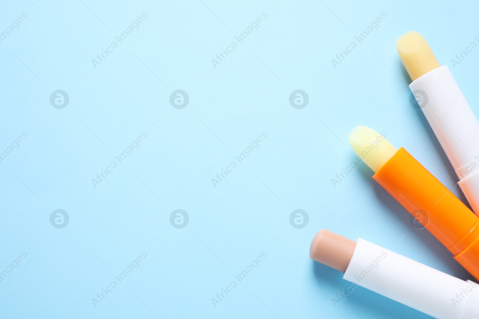 Photo of Hygienic lipsticks on light blue background, flat lay. Space for text