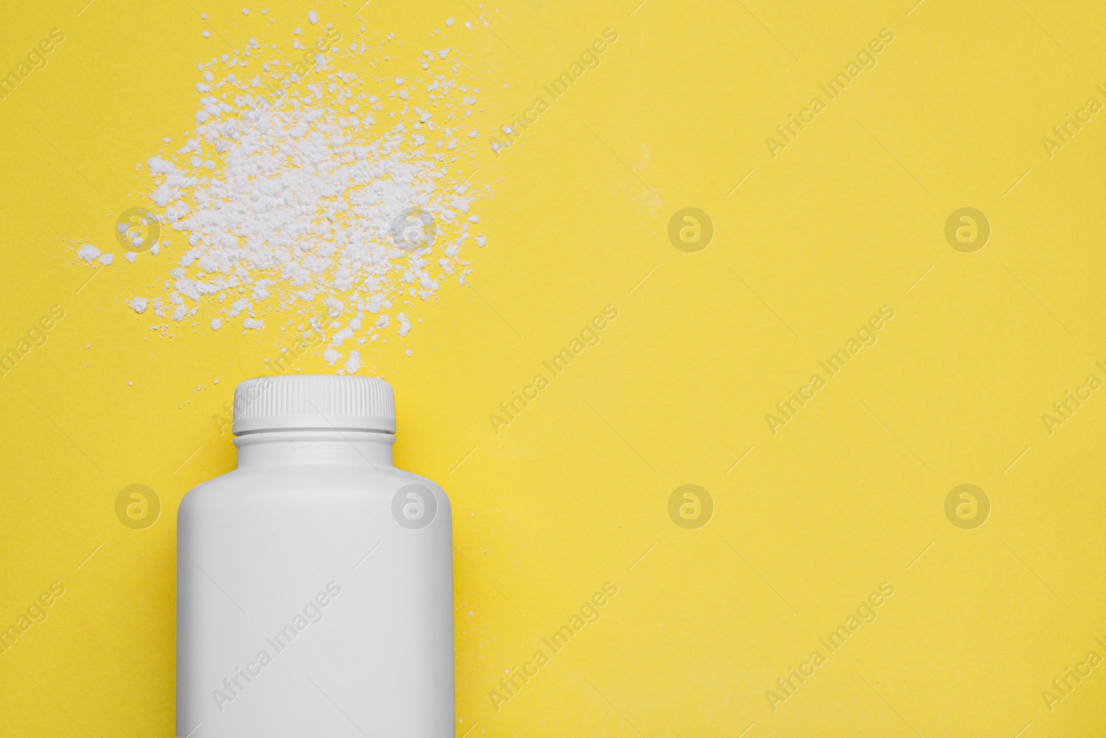 Photo of Bottle and scattered dusting powder on yellow background, top view with space for text. Baby cosmetic product