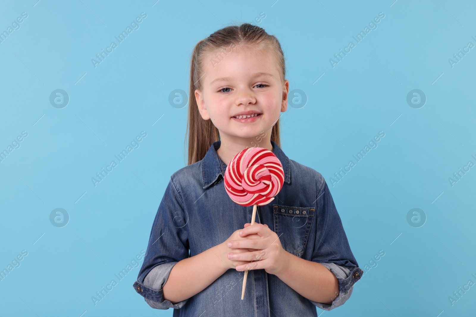 Photo of Happy little girl with bright lollipop swirl on light blue background