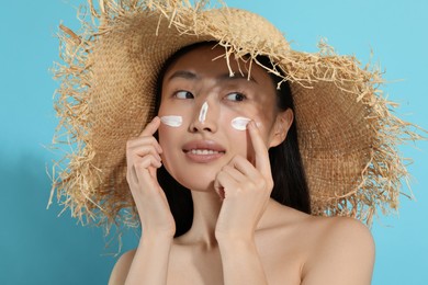 Photo of Beautiful young woman in straw hat with sun protection cream on her face against light blue background