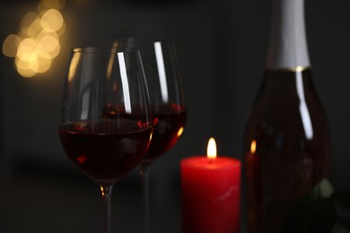 Glasses of red wine and burning candle against blurred lights, space for text. Romantic atmosphere