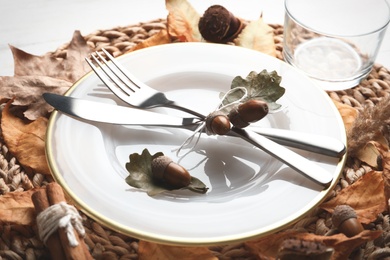 Autumn table setting with dry leaves on wicker mat, closeup