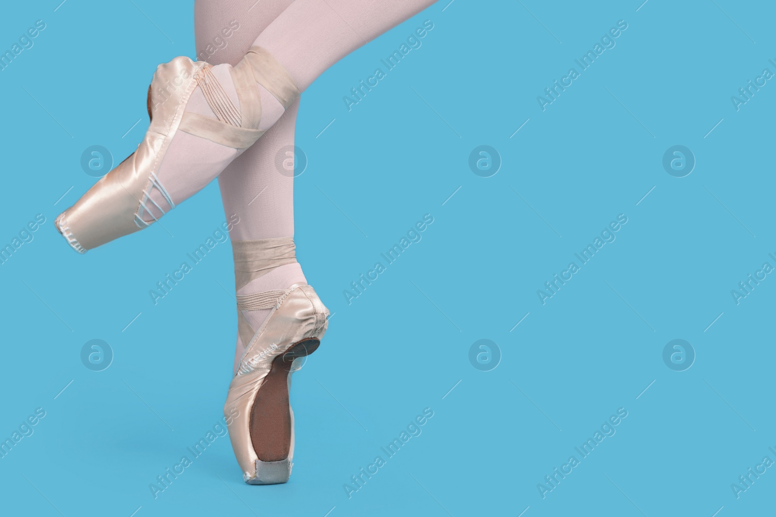 Photo of Young ballerina in pointe shoes practicing dance moves on light blue background, closeup. Space for text