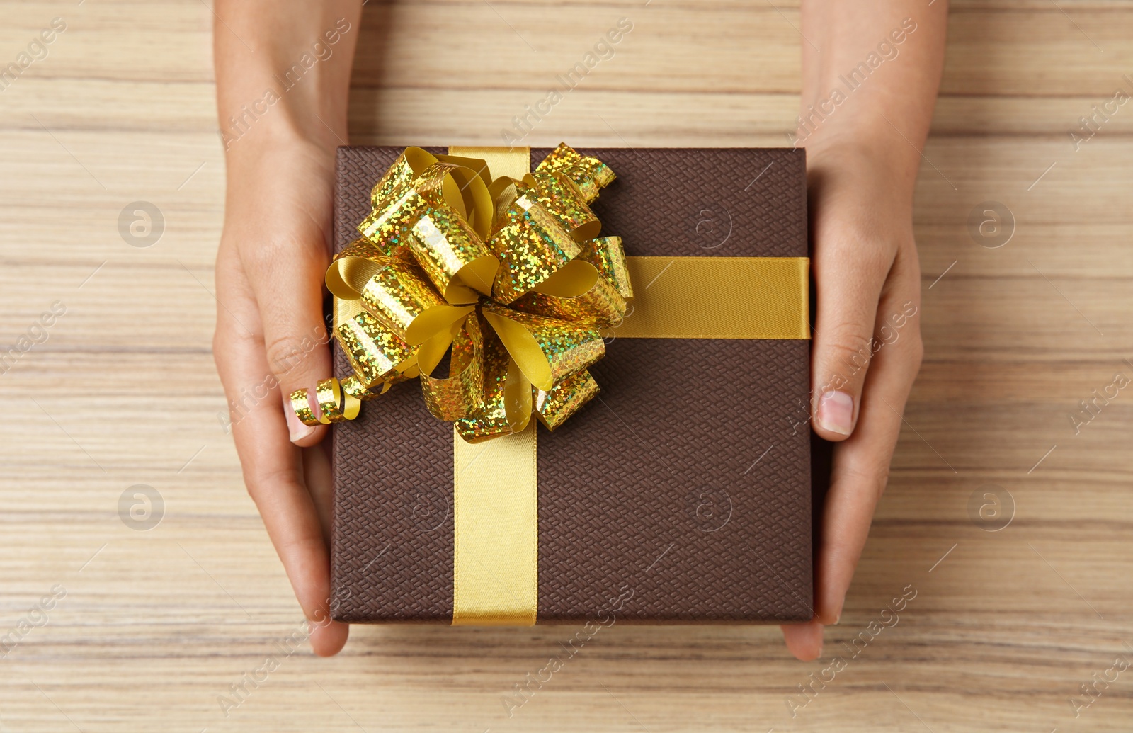 Photo of Woman holding beautiful gift box over wooden table, top view