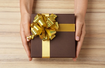 Photo of Woman holding beautiful gift box over wooden table, top view