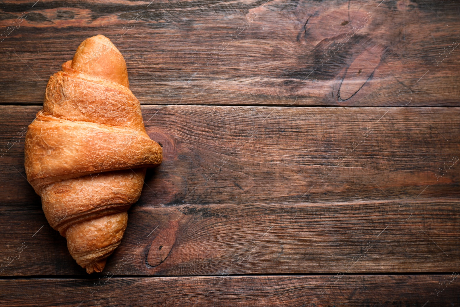 Photo of Tasty fresh croissant on wooden table, top view. Space for text