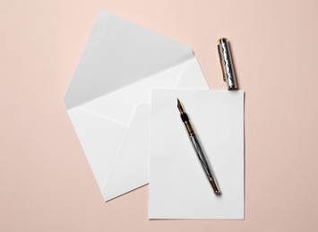 Blank sheet of paper, letter envelope and pen on beige background, top view
