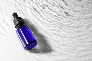 Photo of Bottle of face serum in water on white background, space for text
