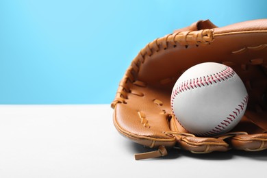 Photo of Baseball glove and ball on white table against color background, closeup. Space for text