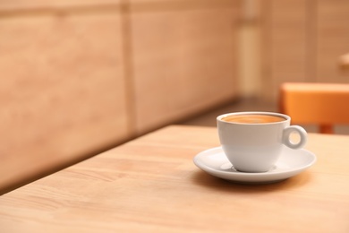 Cup of fresh aromatic coffee on table against blurred background. Space for text