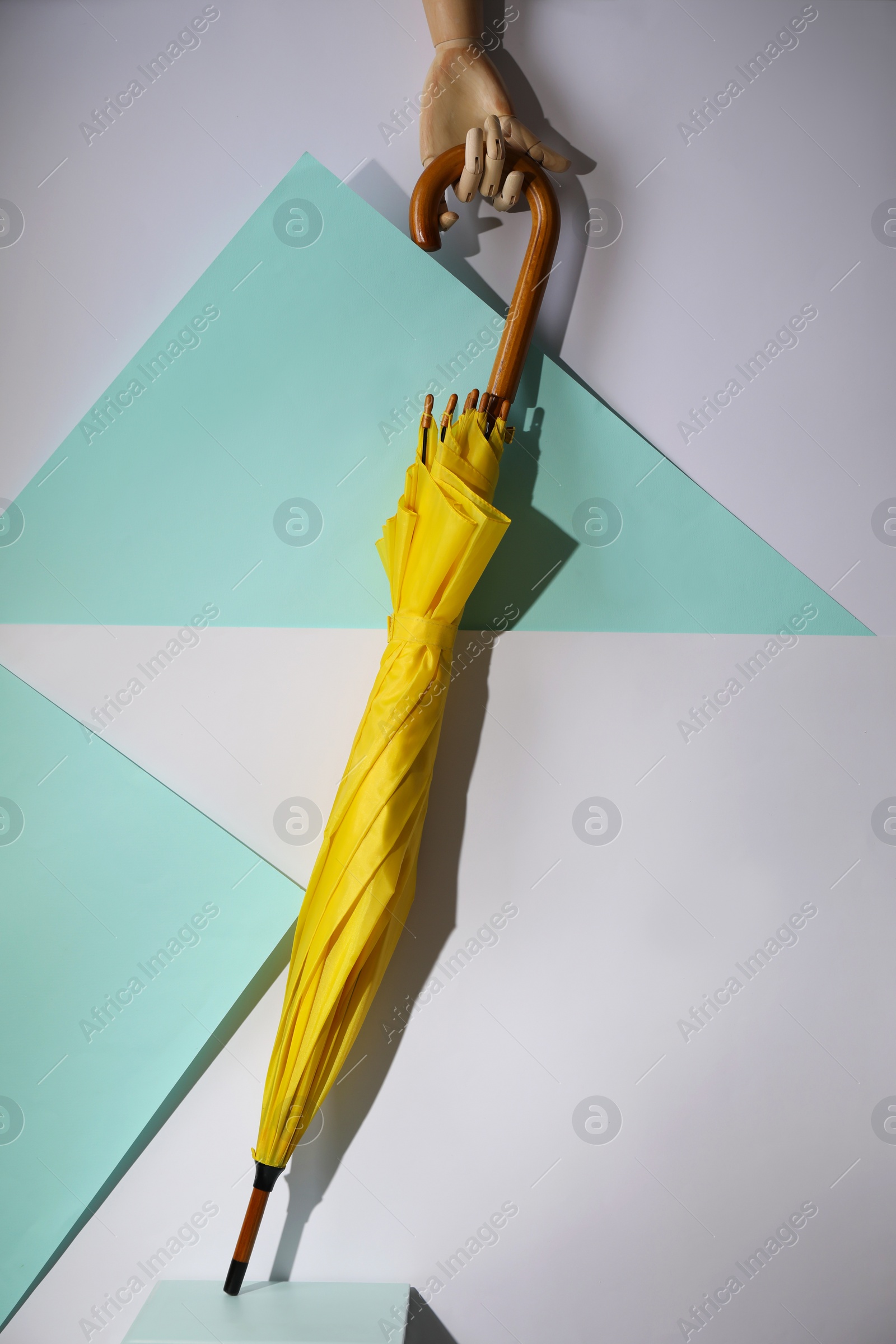 Photo of Wooden hand holding yellow umbrella on color background