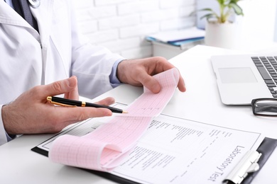 Doctor examining cardiogram at table in clinic, closeup