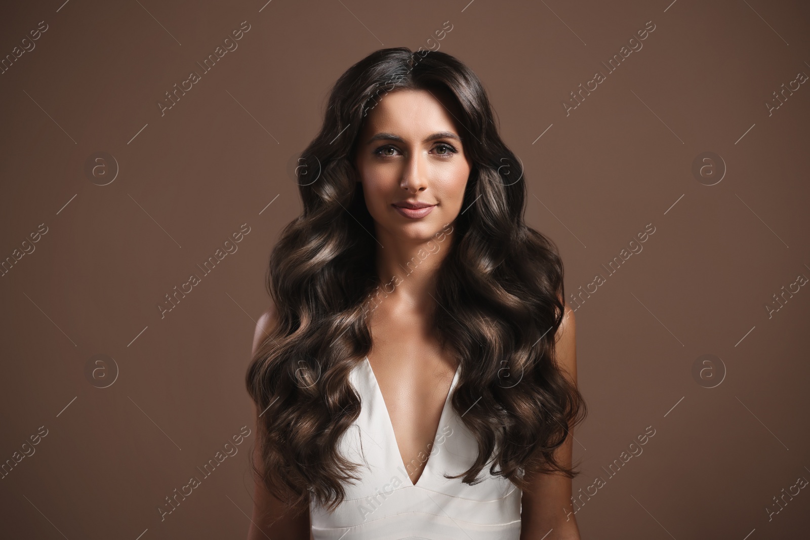 Image of Gorgeous woman with shiny wavy hair on brown background. Professional hairstyling