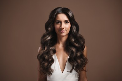 Gorgeous woman with shiny wavy hair on brown background. Professional hairstyling