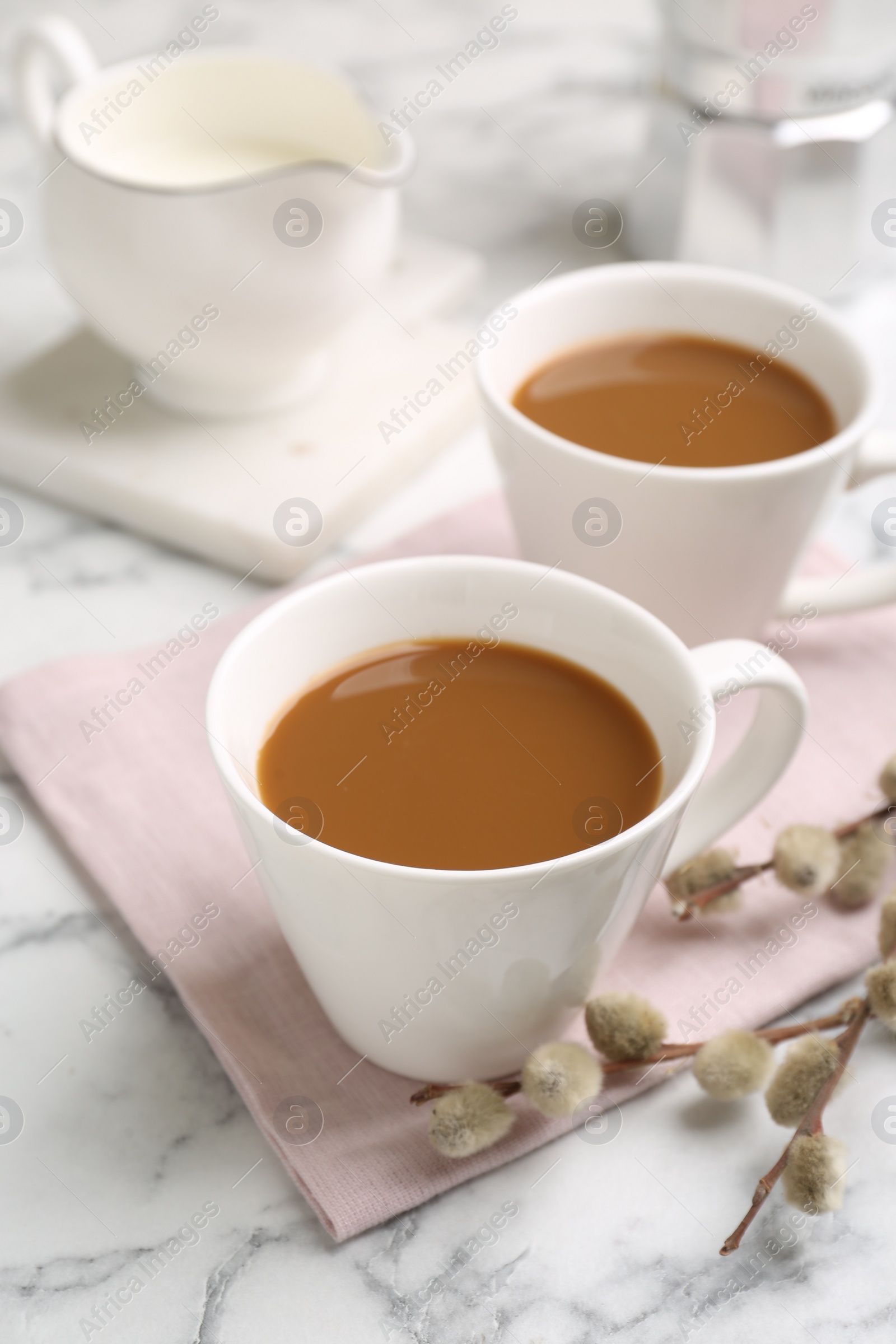 Photo of Cups of hot aromatic coffee and willow branches on white marble table