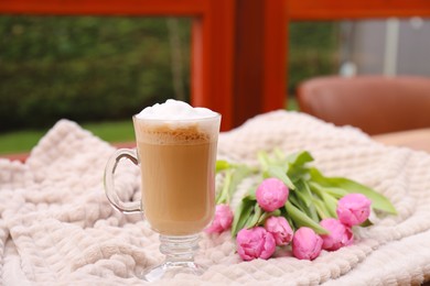 Photo of Glass of delicious cocoa and pink tulips on light blanket at terrace