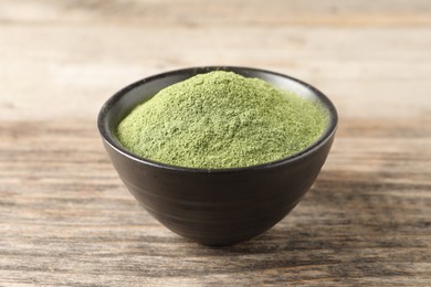 Wheat grass powder in bowl on wooden table, closeup